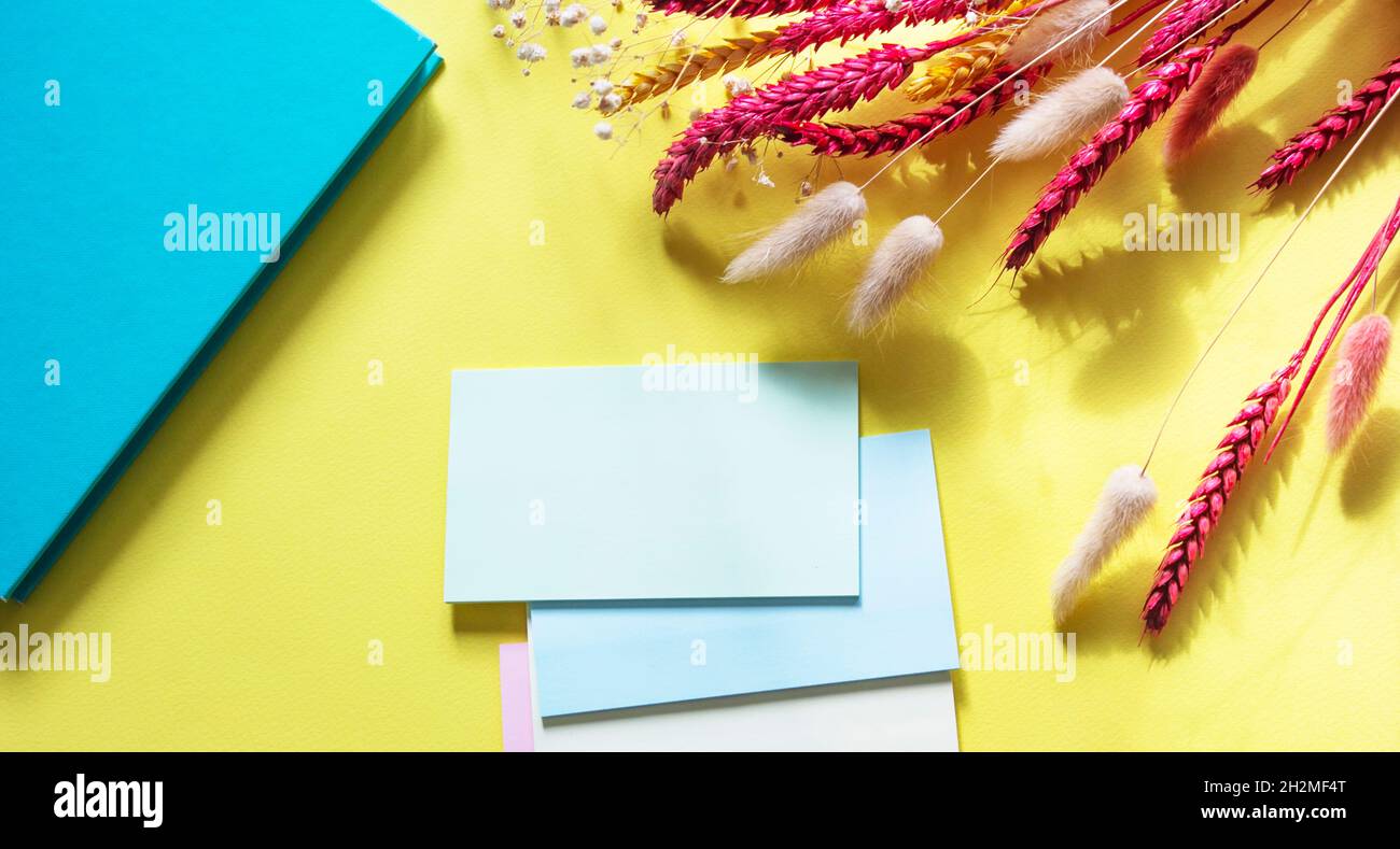Adesivi multicolore vicino alle orecchie di grano e un taccuino turchese su sfondo giallo Foto Stock