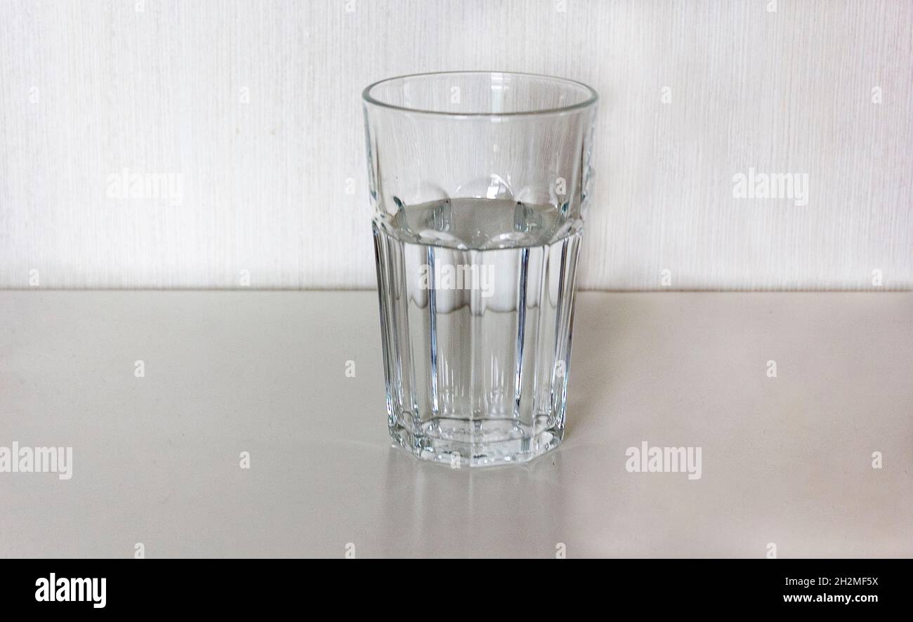 Primo piano di vetro sfaccettato con acqua potabile su tavola bianca con sfondo chiaro Foto Stock