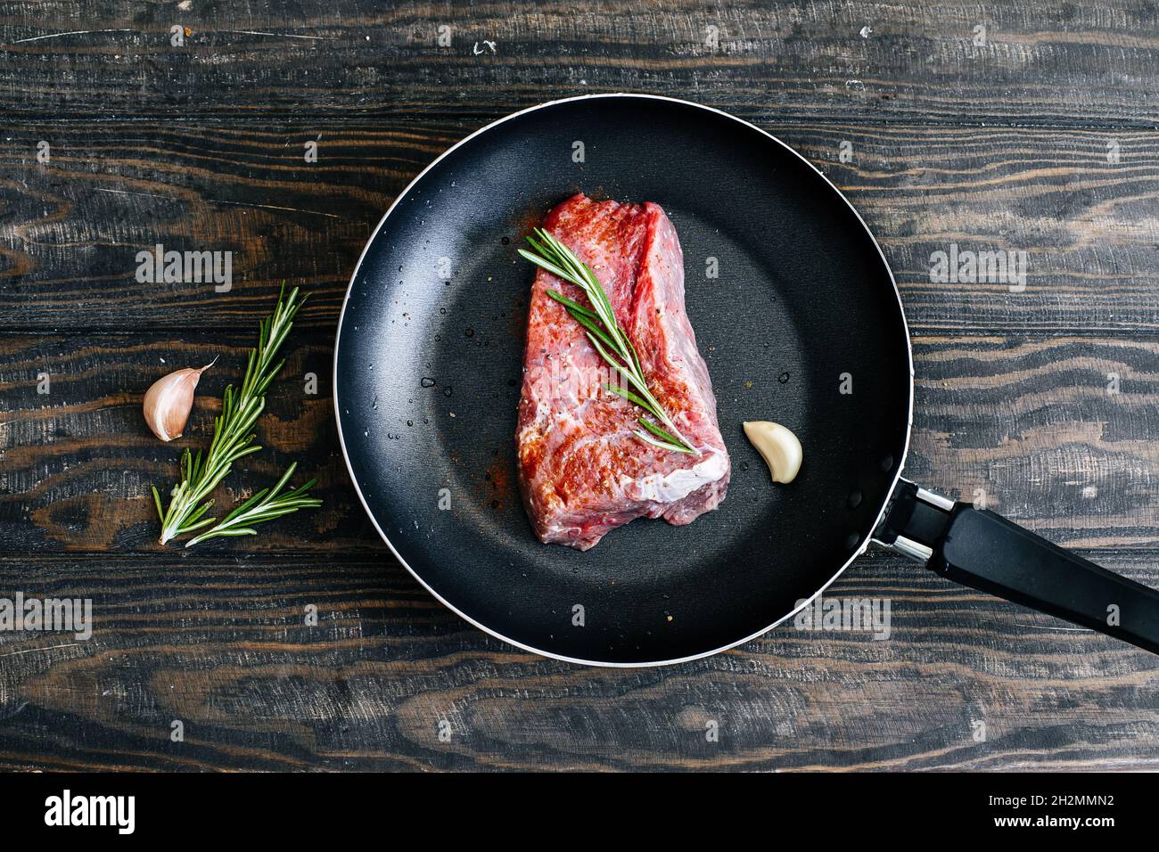 Bistecca di manzo crudo con rosmarino in una padella con vista sul tavolo in legno Foto Stock