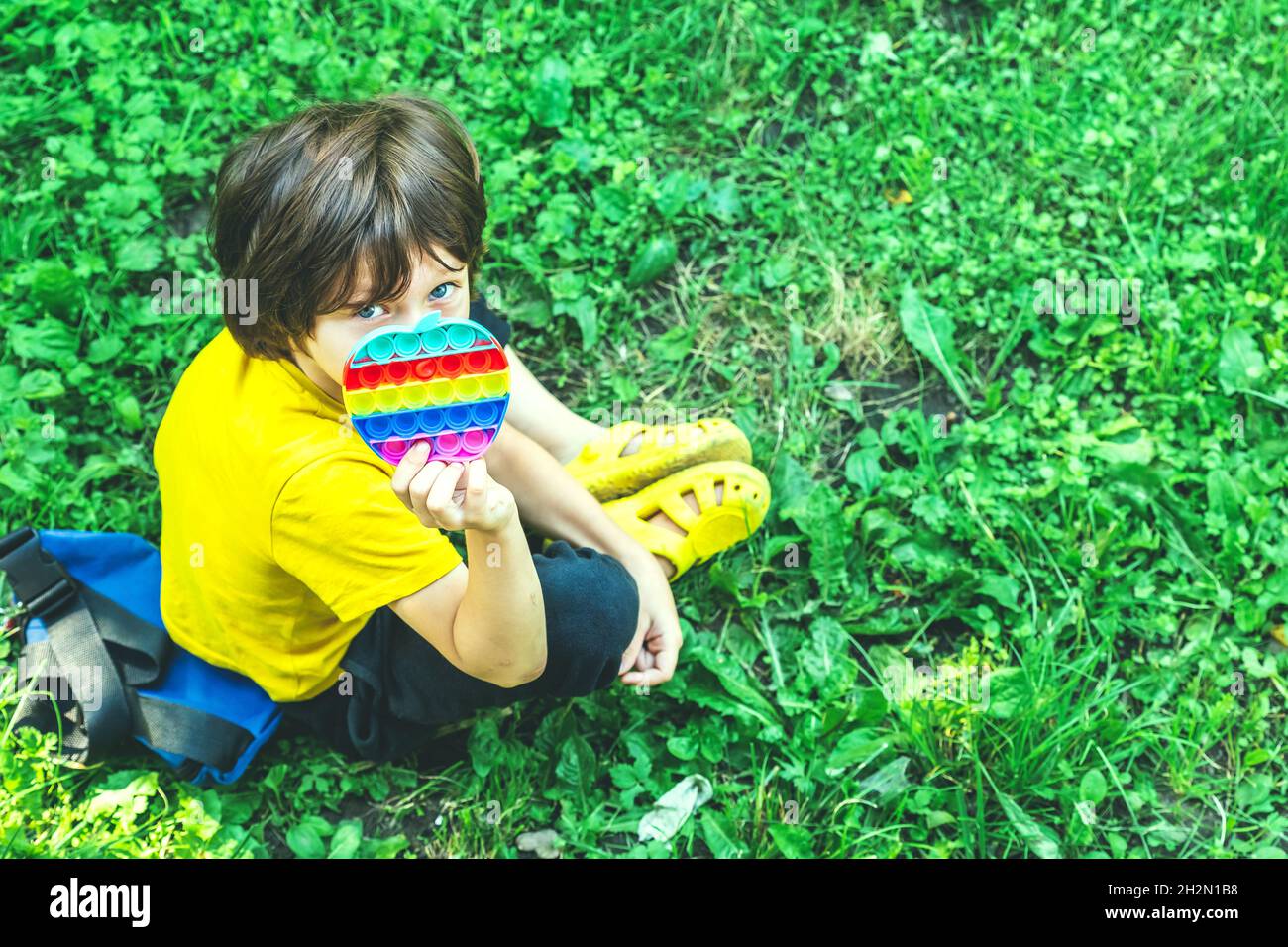 Carino ragazzo del preschooler che gioca con il giocattolo flessibile sensoriale del fidget del Pop IT seduto sull'erba all'aperto. Attività per bambini, sviluppo mentale. Selettivo Foto Stock