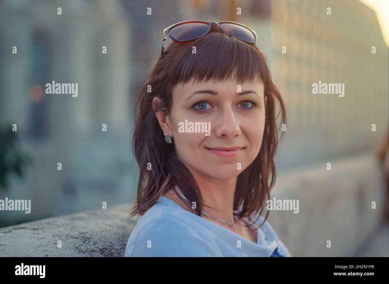 Primo piano ritratto di giovane allegra bella donna con capelli scuri, occhi grigi e occhiali da sole sulla testa, guardando la macchina fotografica, posando e sorridendo all'aperto dentro Foto Stock