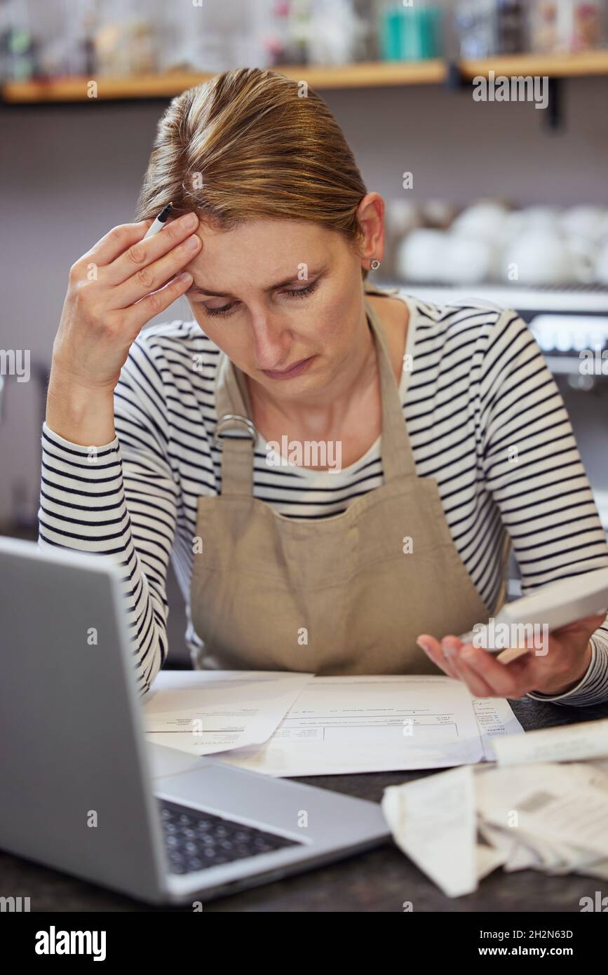 Donna preoccupata Proprietario di Coffee Shop in difficoltà finanziaria cercando Attraverso le fatture con notebook e calcolatrice Foto Stock