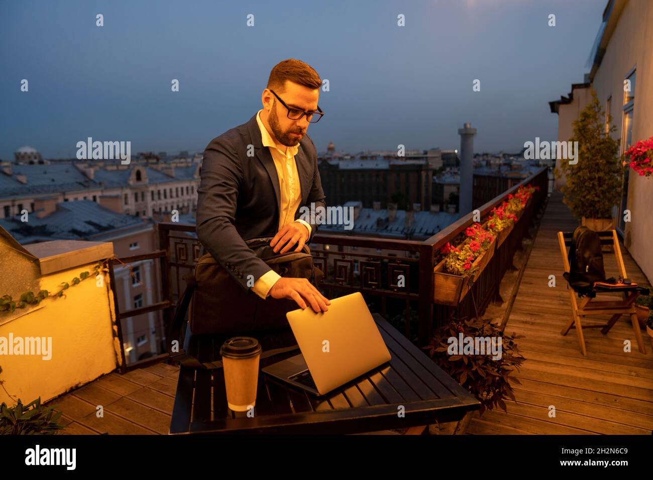Uomo d'affari che chiude il computer portatile sul tavolo in balcone durante la notte Foto Stock
