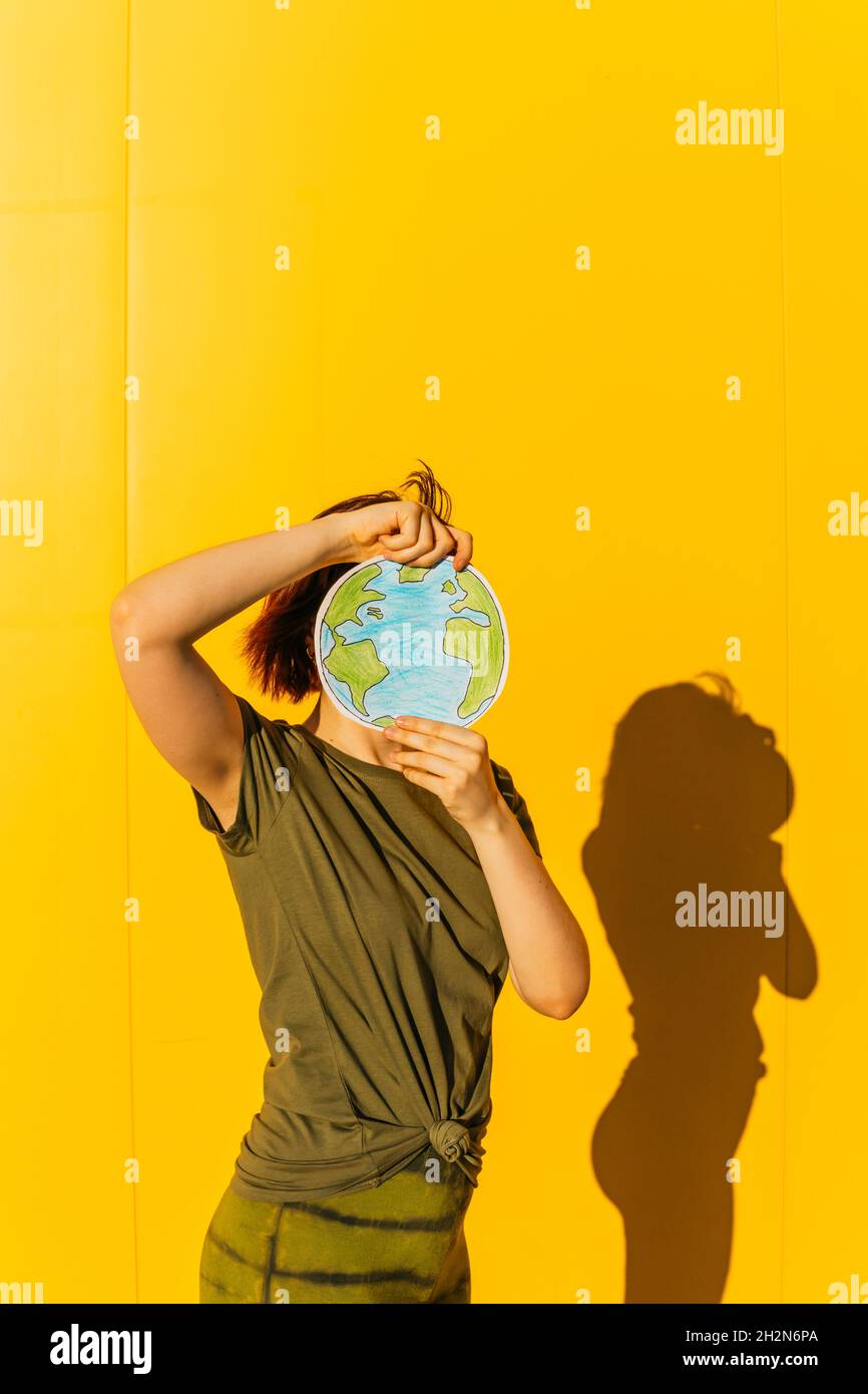 Donna che tiene carta terra pianeta di fronte al muro giallo Foto Stock