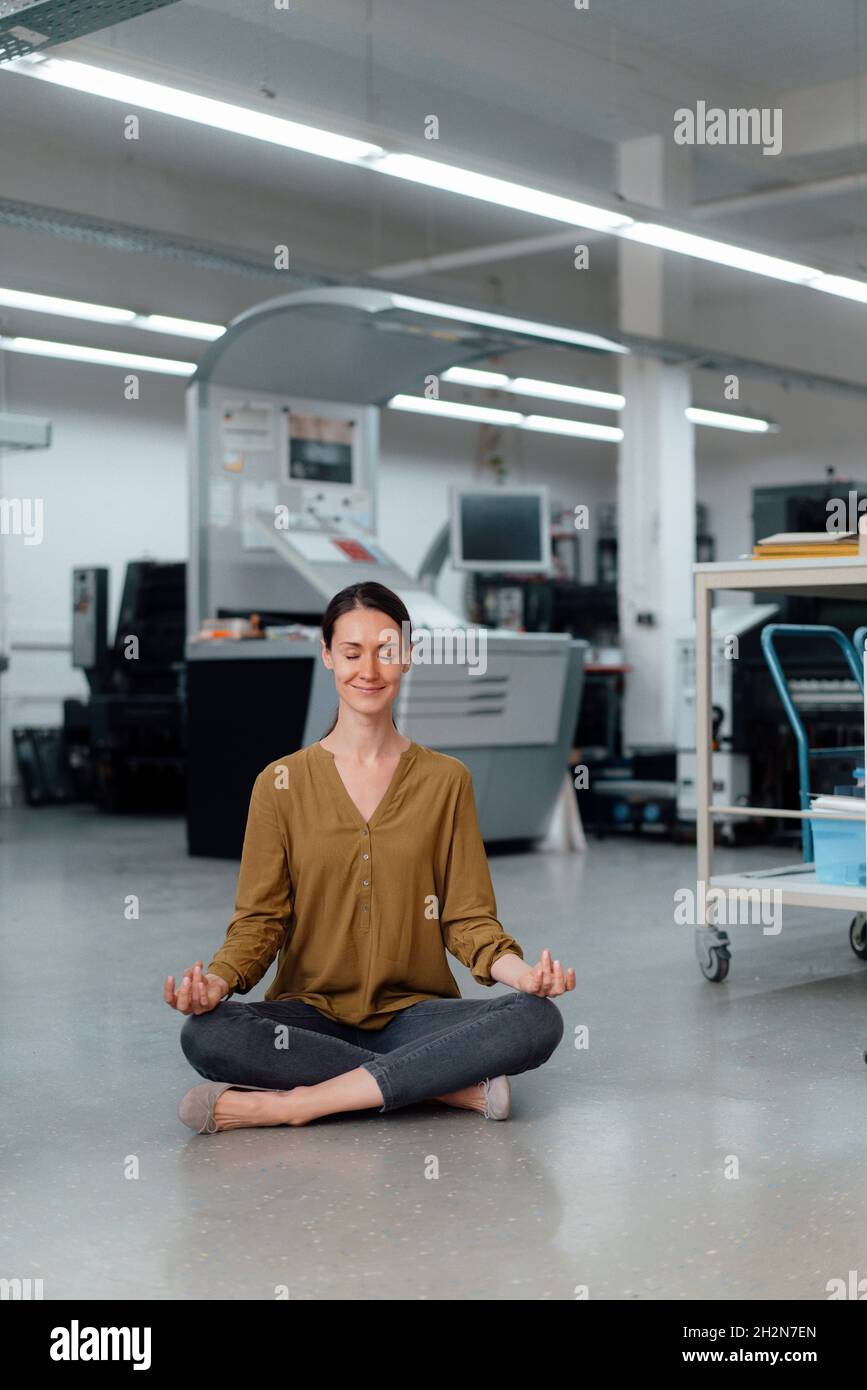 Donna d'affari che pratica yoga in laboratorio Foto Stock