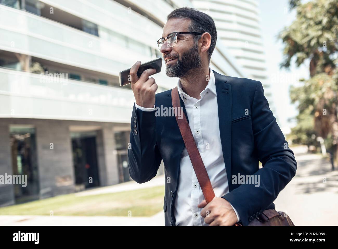 Uomo d'affari con borsa a tracolla che invia messaggi vocali tramite smartphone Foto Stock