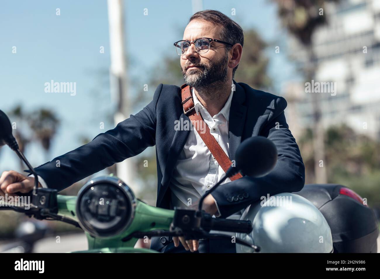 Uomo d'affari con casco e borsa a tracolla seduta su scooter a motore Foto Stock