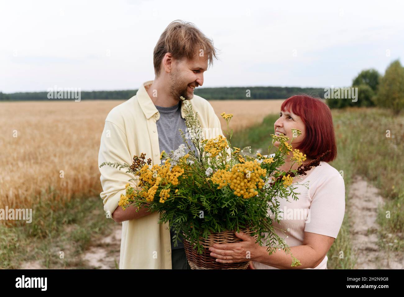 Coppia senior con cesto di fiori di tansy e rastrello a piedi dal grano Foto Stock