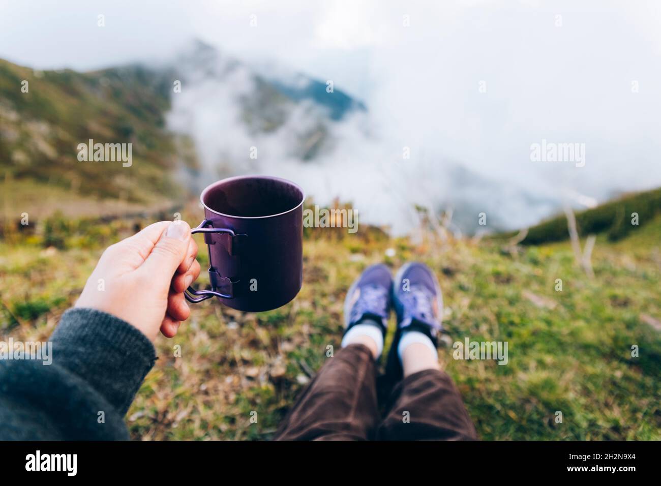 Donna che tiene una tazza di tè mentre si siede sulla montagna Foto Stock