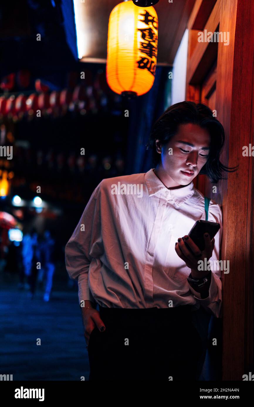 Giovane uomo in piedi con mano in tasca utilizzando il telefono cellulare di notte Foto Stock