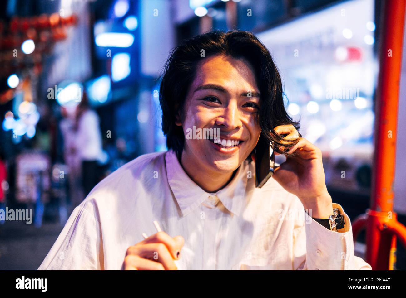 Felice giovane uomo che parla al telefono cellulare in città illuminata Foto Stock