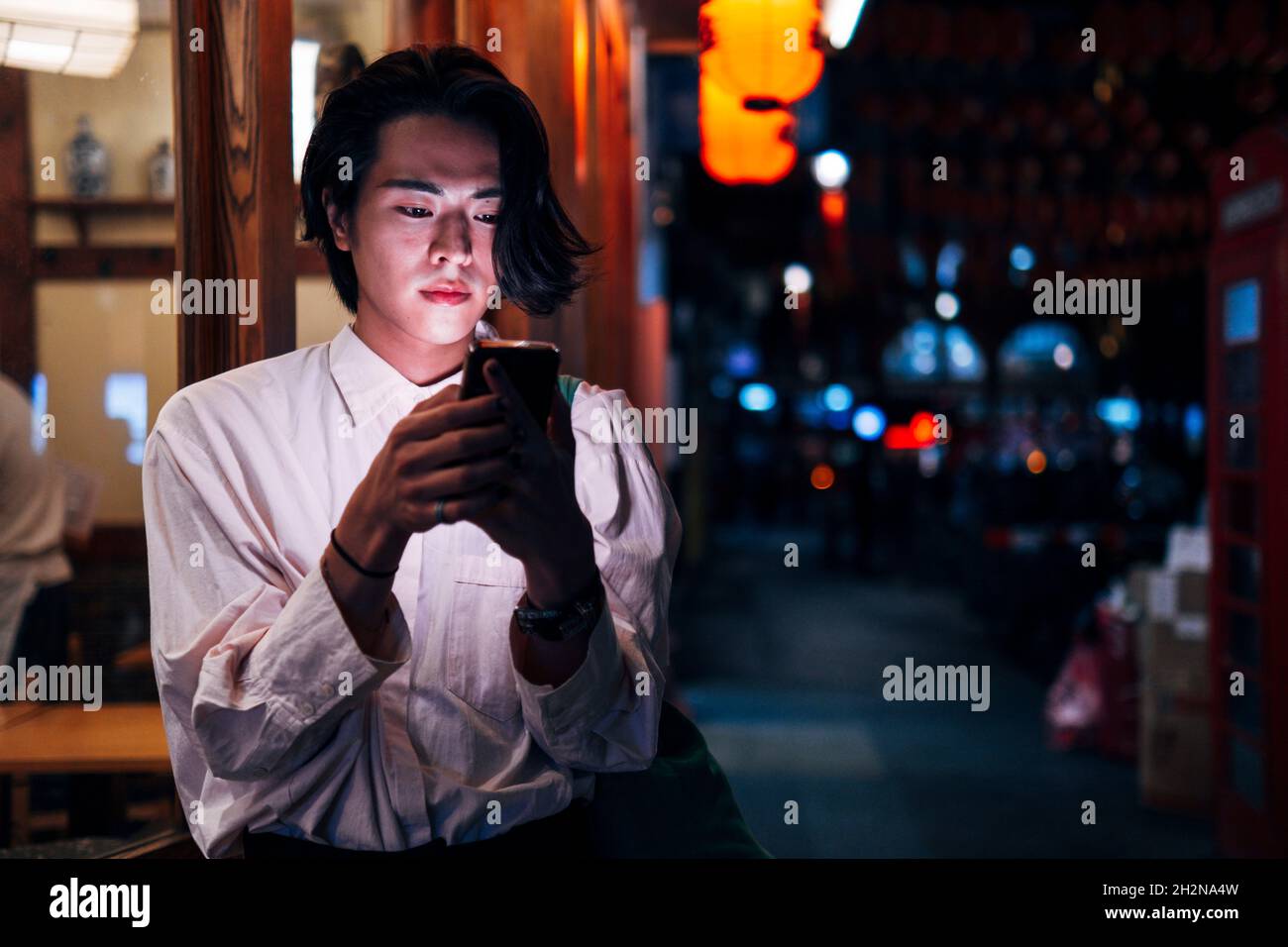 Giovane uomo con capelli neri usando lo smartphone in città di notte Foto Stock