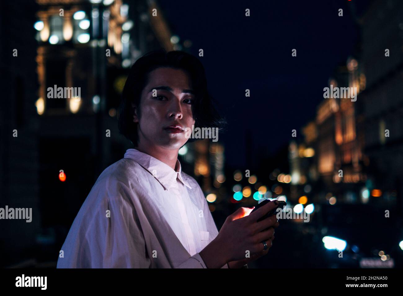 Giovane uomo con smartphone in città illuminata di notte Foto Stock