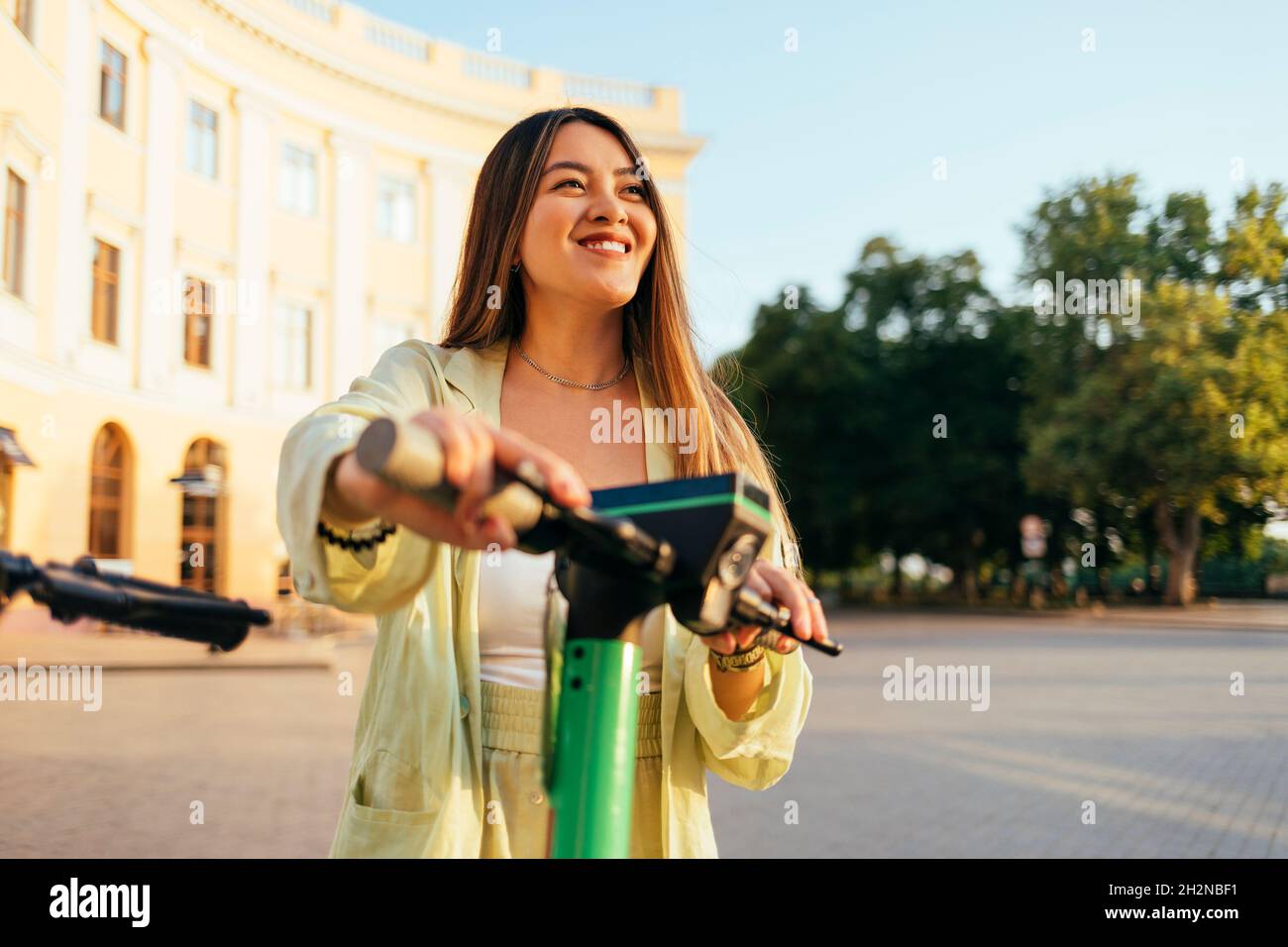 Giovane donna sorridente con scooter elettrico a spinta in città Foto Stock