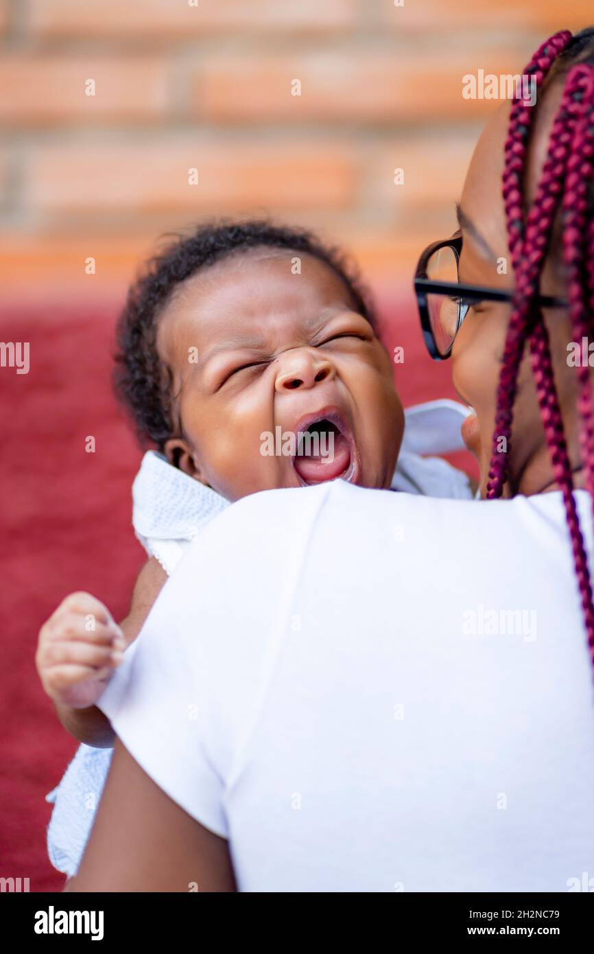 Il bambino sbadigia mentre è portato dalla madre Foto Stock