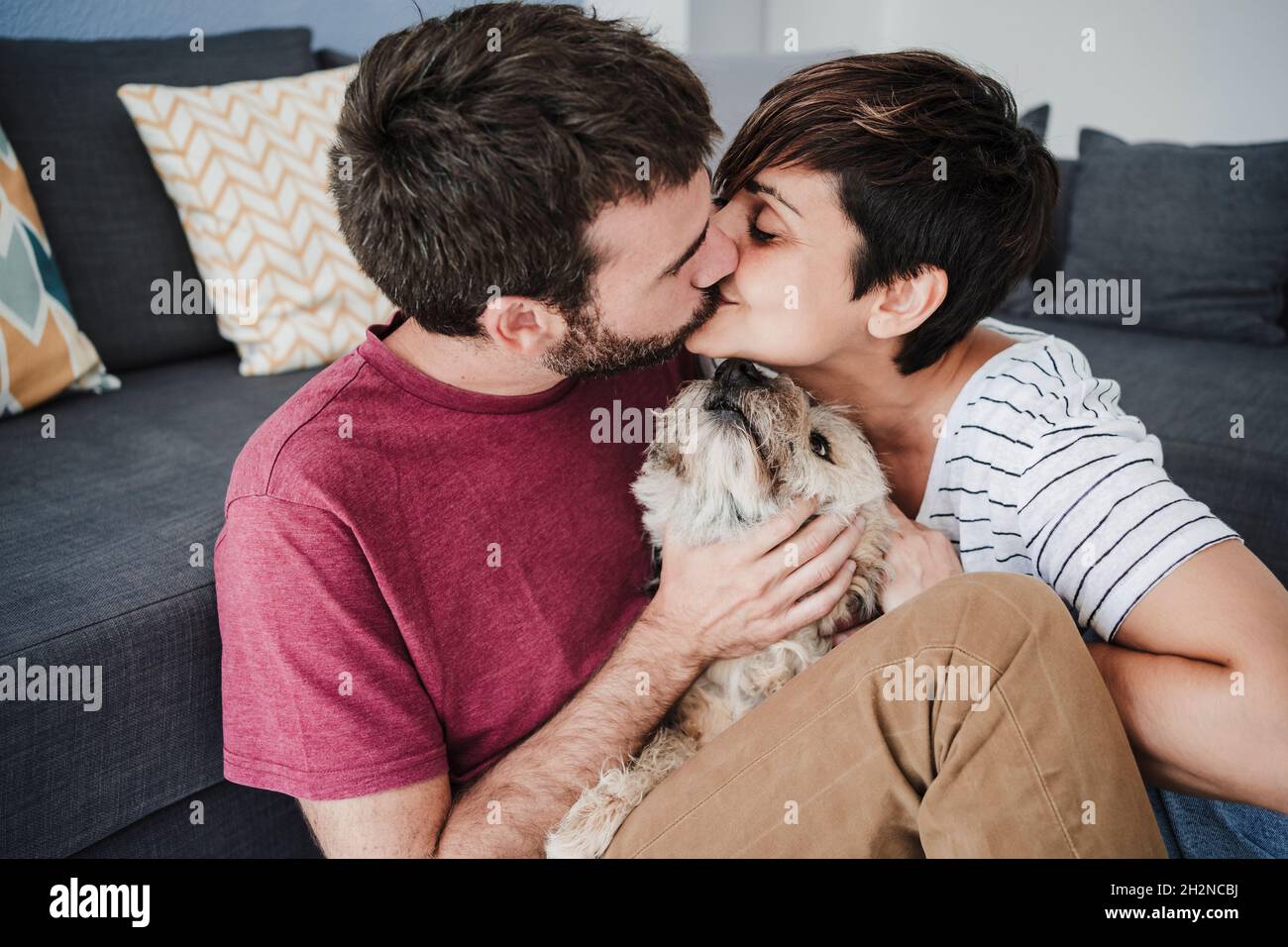 Una coppia affettuosa bacia mentre si siede con cane di razza mista a casa Foto Stock