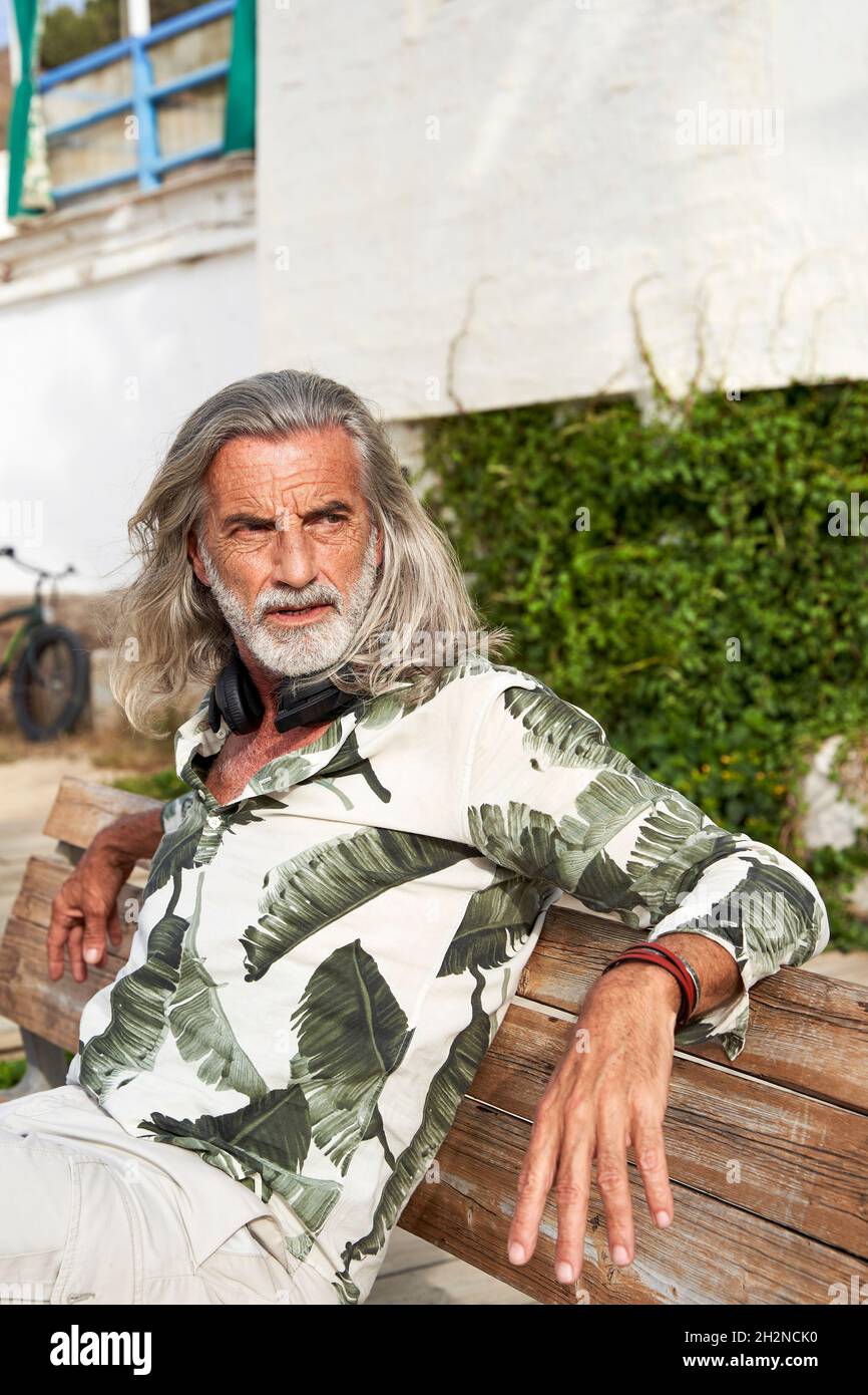 Uomo Hipster con lunghi capelli grigi seduti su panca Foto Stock