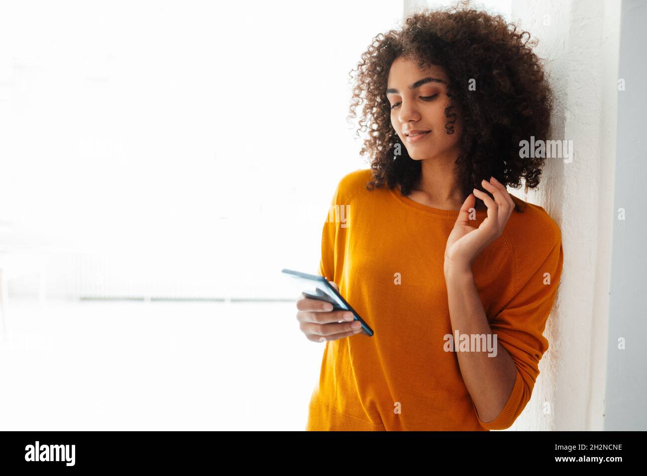 Afro giovane donna messaggi di testo tramite smartphone a casa Foto Stock