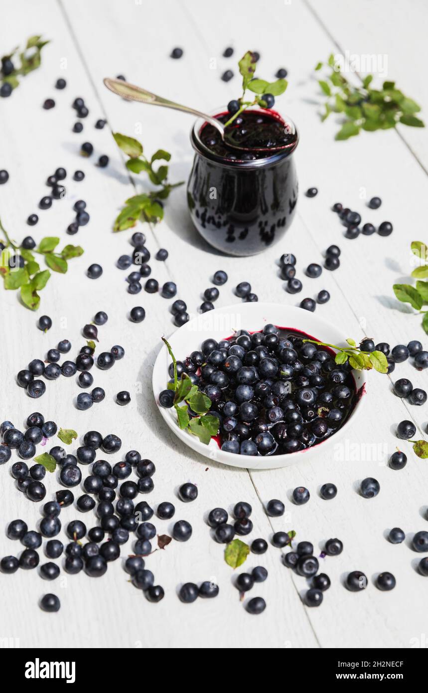 Mirtilli crudi e bicchiere di marmellata di mirtilli fatta in casa su tavola bianca Foto Stock
