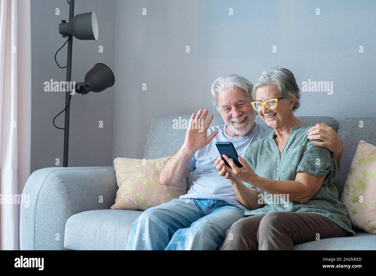 Sorridente uomo anziano che ondeggiava durante la videochiamata da parte della donna a casa Foto Stock