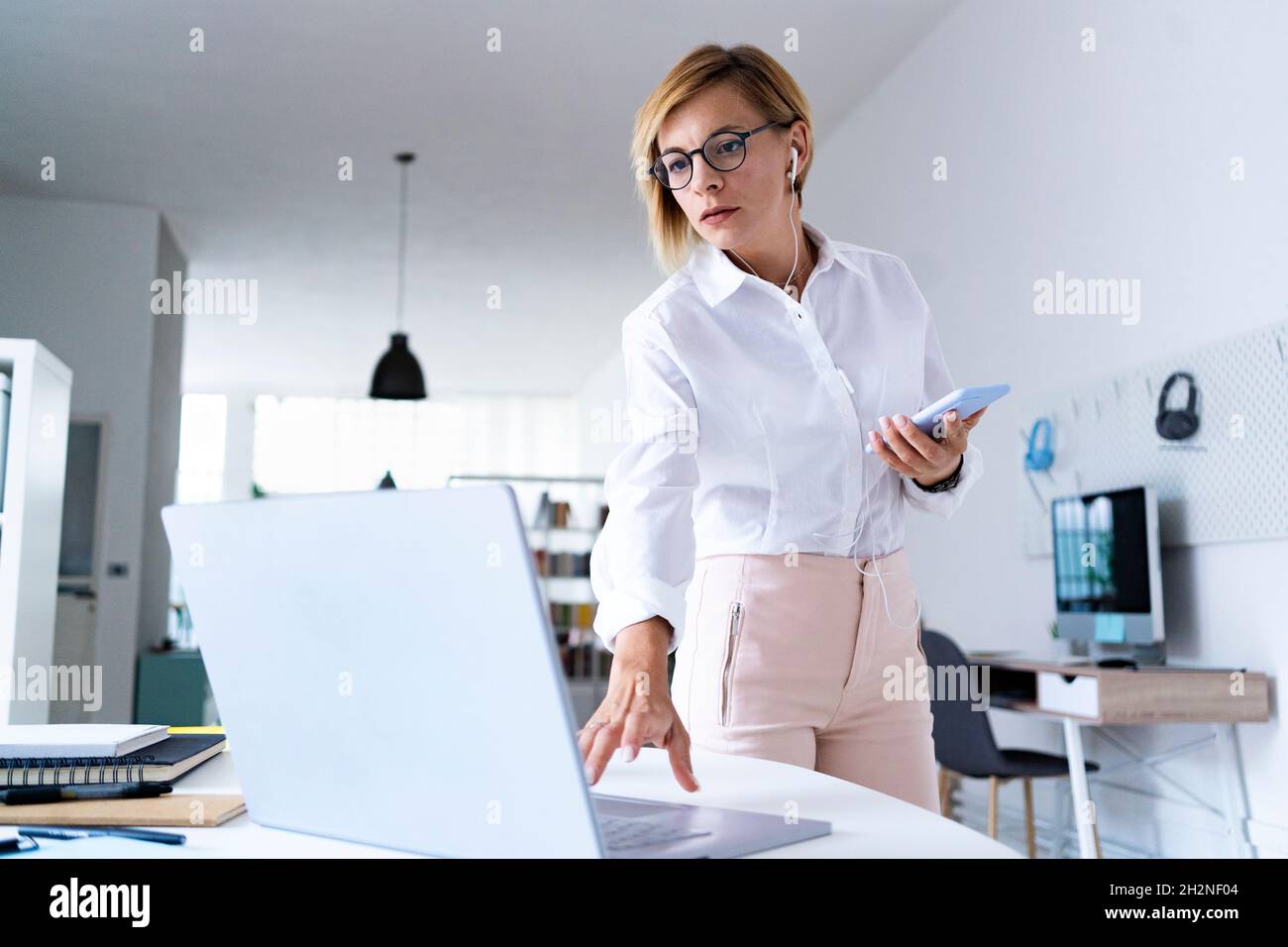 Donna d'affari con la tazza che invia la posta vocale tramite smartphone in ufficio Foto Stock