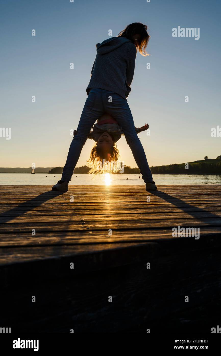 Madre e figlia che giocano sul molo durante il tramonto Foto Stock