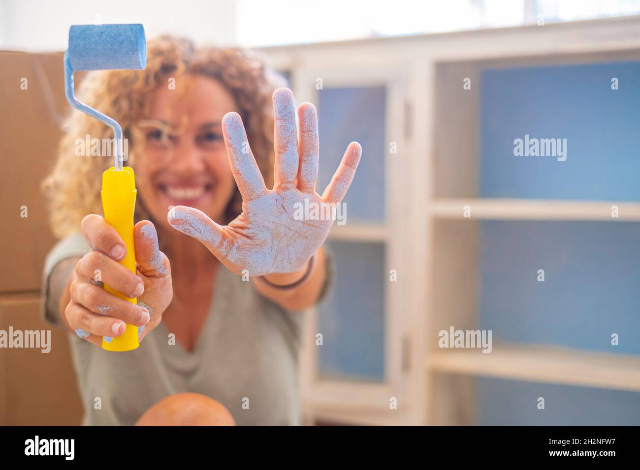 Donna sorridente con rullo di vernice e vernice blu a portata di mano a casa Foto Stock