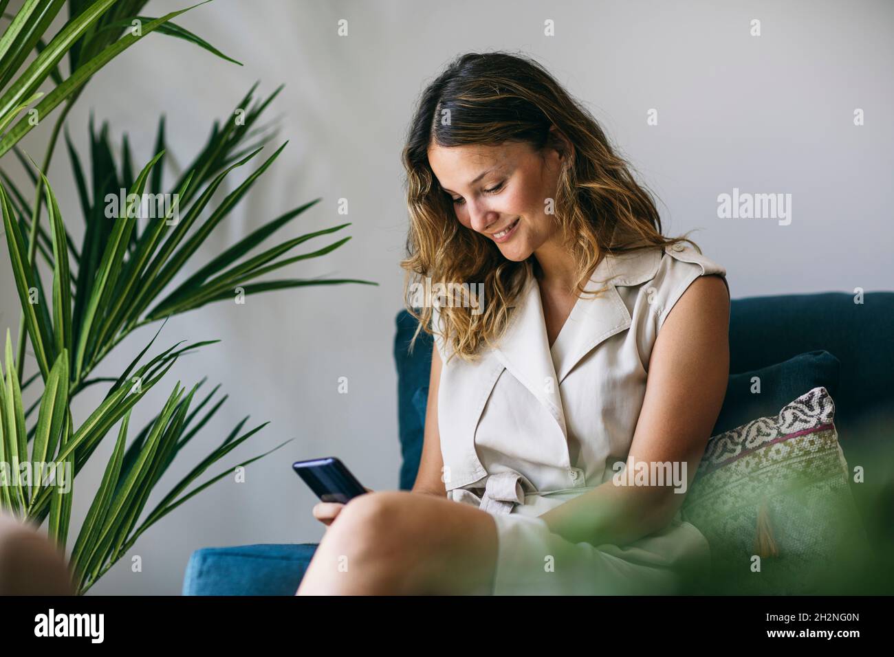 Donna sorridente che invia messaggi di testo tramite telefono cellulare mentre si siede sul divano Foto Stock