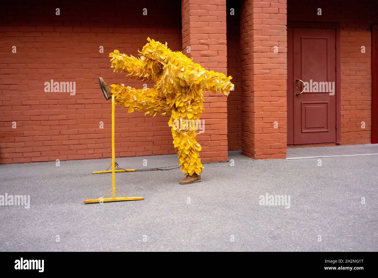 Donna in costume foglia tenendo gamba su strada barricata da muro di mattoni Foto Stock