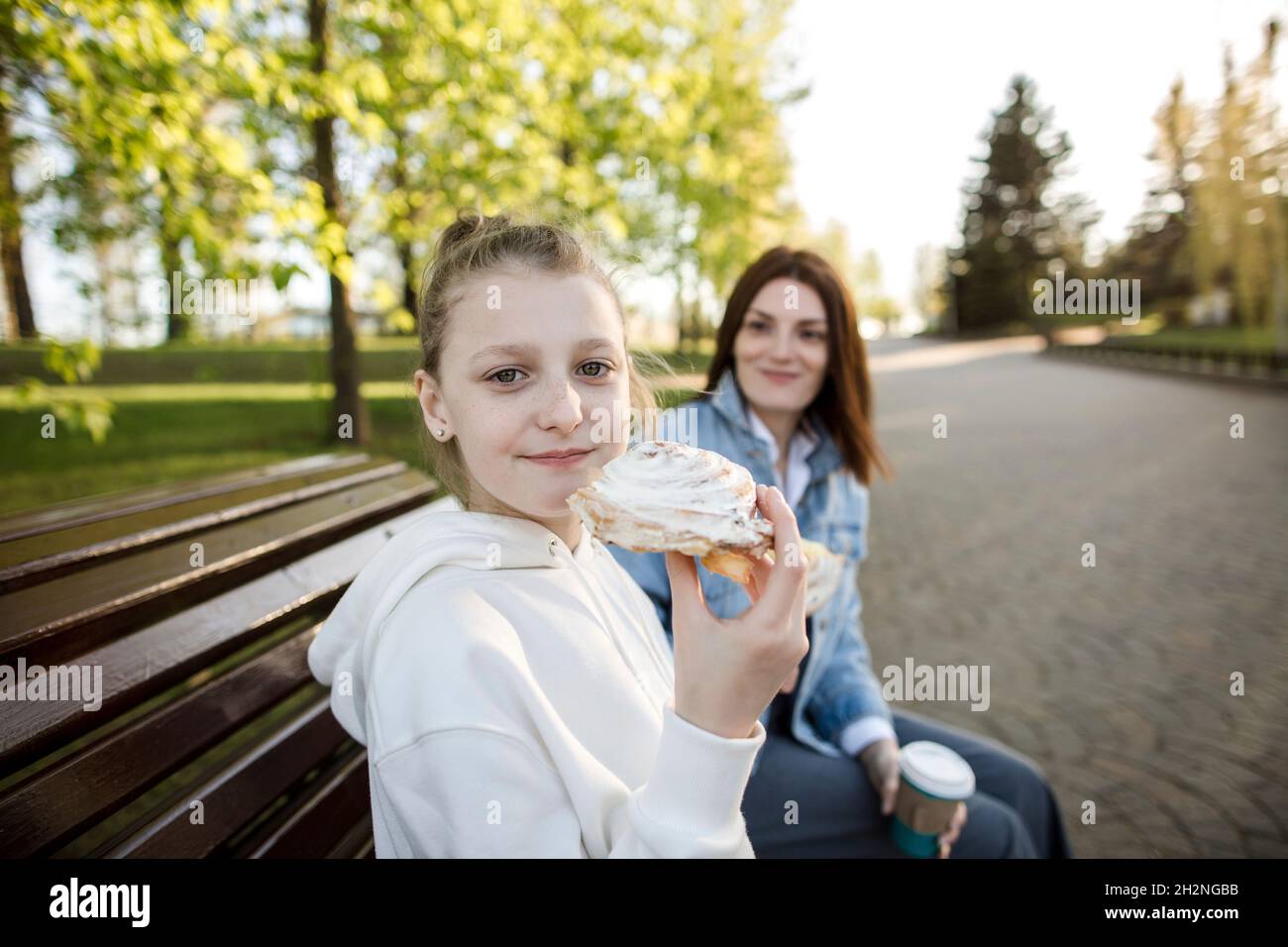 Ragazza che ha cibo dolce mentre si siede con la madre su panca Foto Stock