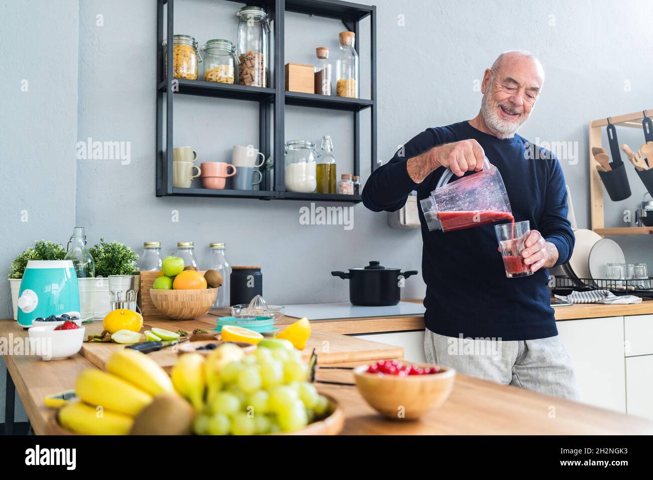 Uomo sorridente che prepara il frullato nella centrifuga elettrica al banco della cucina Foto Stock