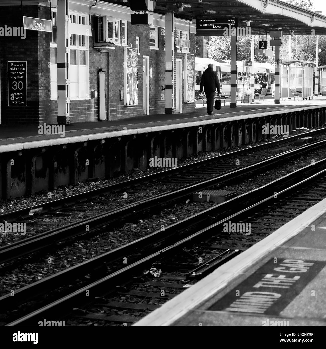 Binario ferroviario che attraversa la stazione di Epsom a Surrey con una persona che cammina lungo una piattaforma vuota Foto Stock