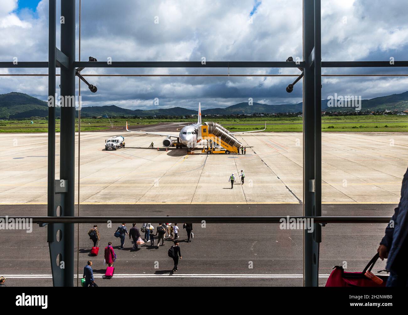 Attraverso la finestra del terminal persone a piedi per caricare in un jet fuori sul tarmac a Lien Khuong Airport da lat. Foto Stock