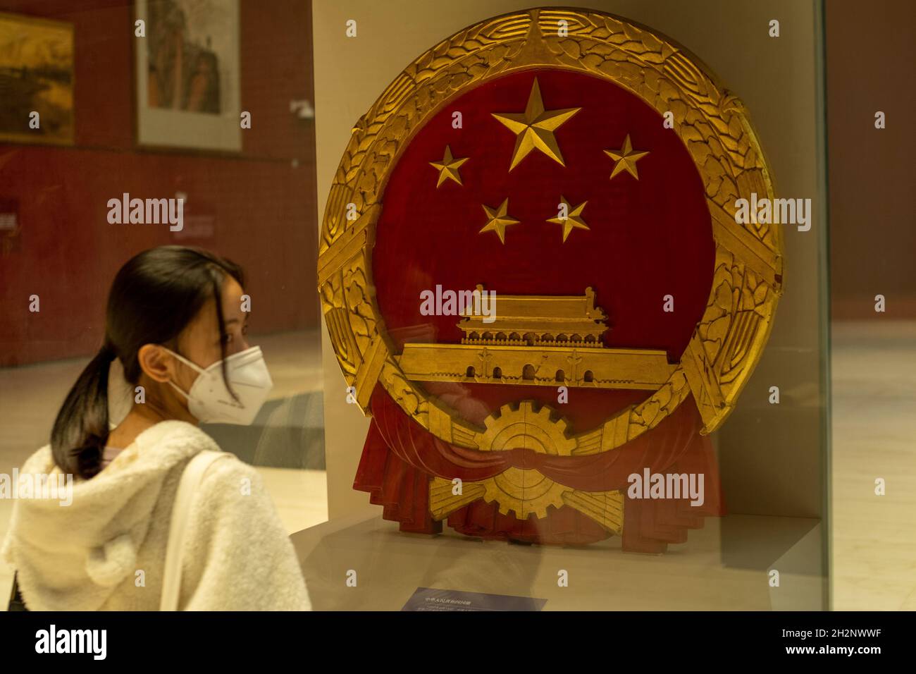 La ragazza cinese passa accanto all'emblema nazionale della Repubblica popolare Cinese nel Museo Nazionale di Pechino, Cina. 23 ottobre 2021 Foto Stock