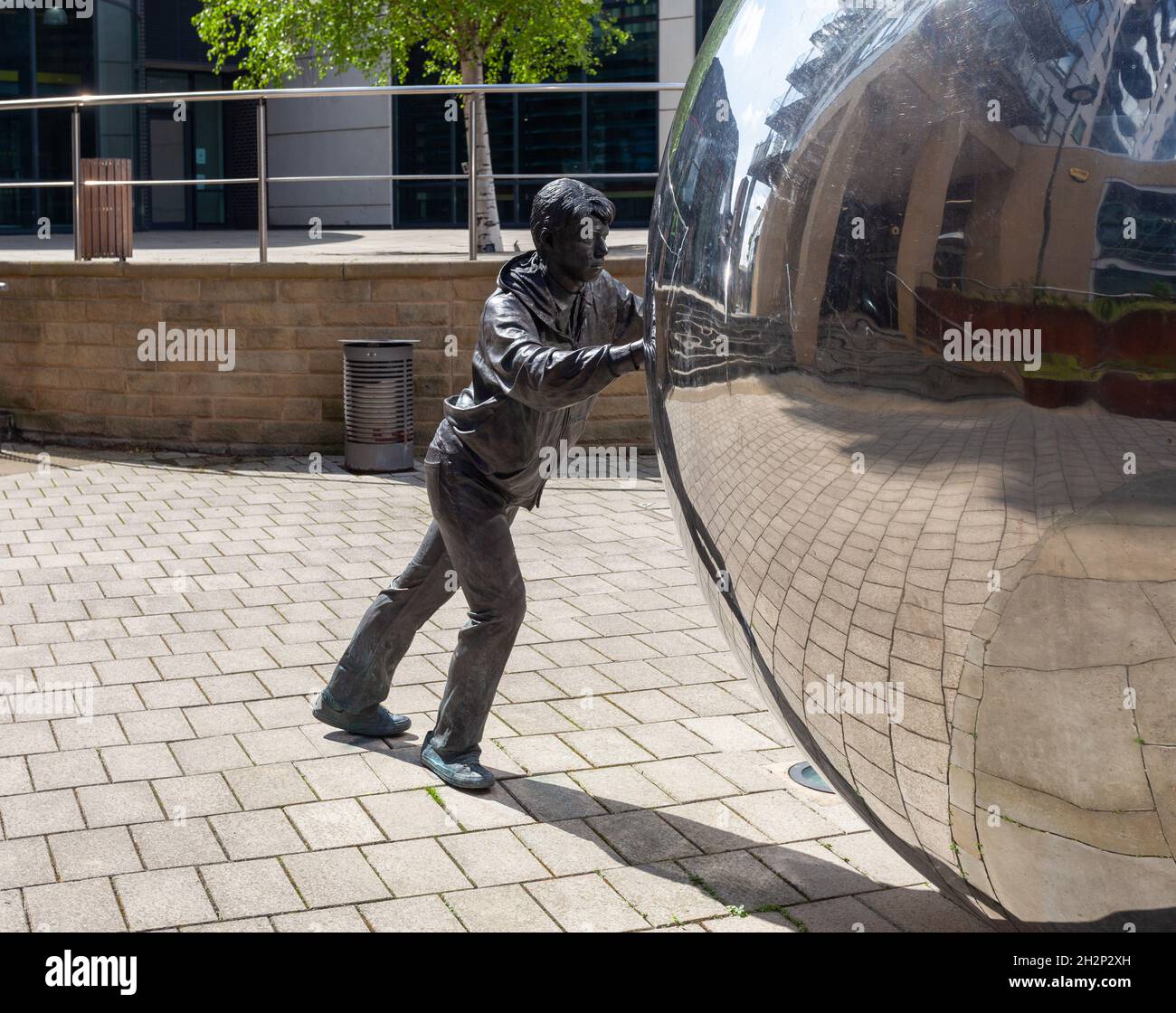 Un approccio riflessivo - scultura di un ragazzo che spinge una sfera riflettente al Clarence Dock, nel centro di Leeds Foto Stock