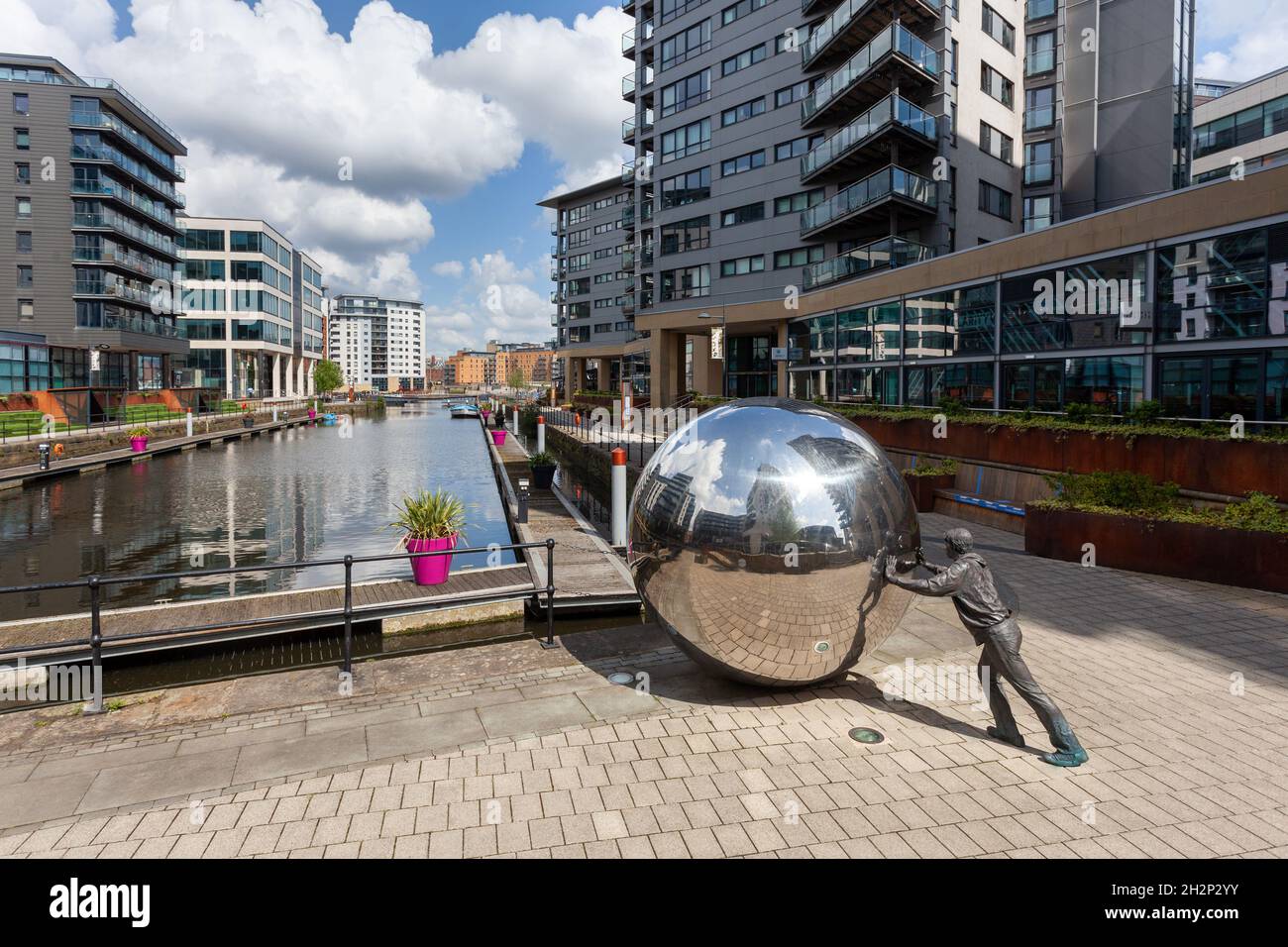 Un approccio riflessivo - scultura di un ragazzo che spinge una sfera riflettente al Clarence Dock, nel centro di Leeds Foto Stock