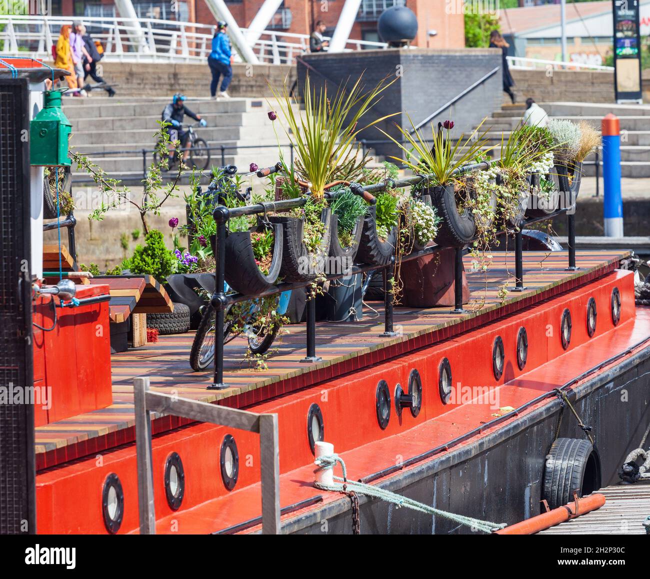 Primo piano di una chiatta del canale ormeggiata al molo di Leeds con piantatrici sul ponte e rotaie che crescono in pneumatici auto riciclati Foto Stock