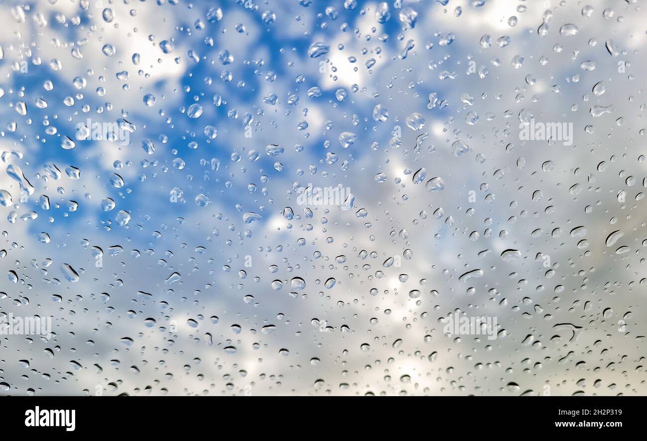 Gocce di pioggia su vetro con cielo blu e sfondo bianco nuvola Foto Stock