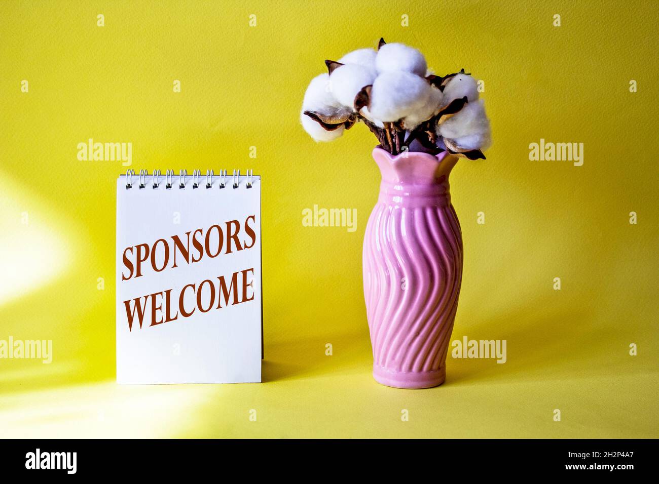 BENVENUTO SPONSOR parole scritte su blocco note con bouquet di cotone Foto Stock