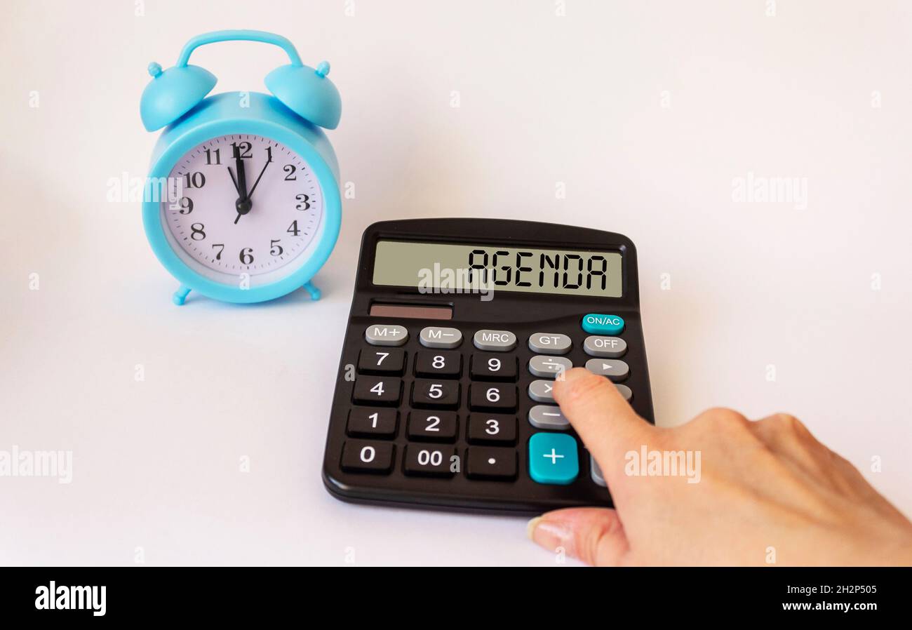 Una mano femminile si trova sulla calcolatrice con il testo sul display AGENDA, su uno sfondo bianco c'è una sveglia Foto Stock