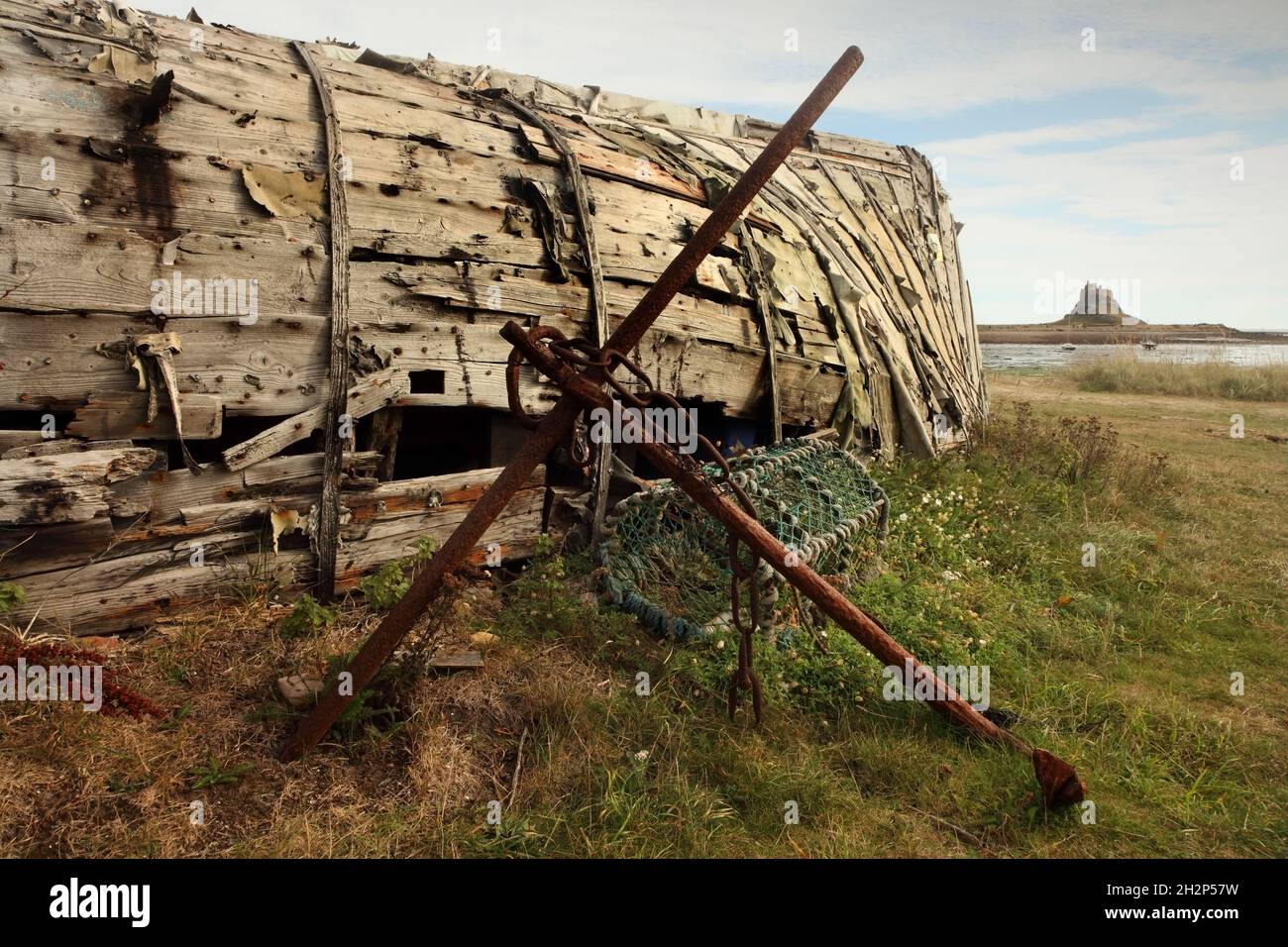 Vecchia ancora, scafo in legno e vaso di aragosta, con il 16 ° secolo Lindisfarne Castello in lontananza, Holy Island, Northumberland, Regno Unito. Foto Stock