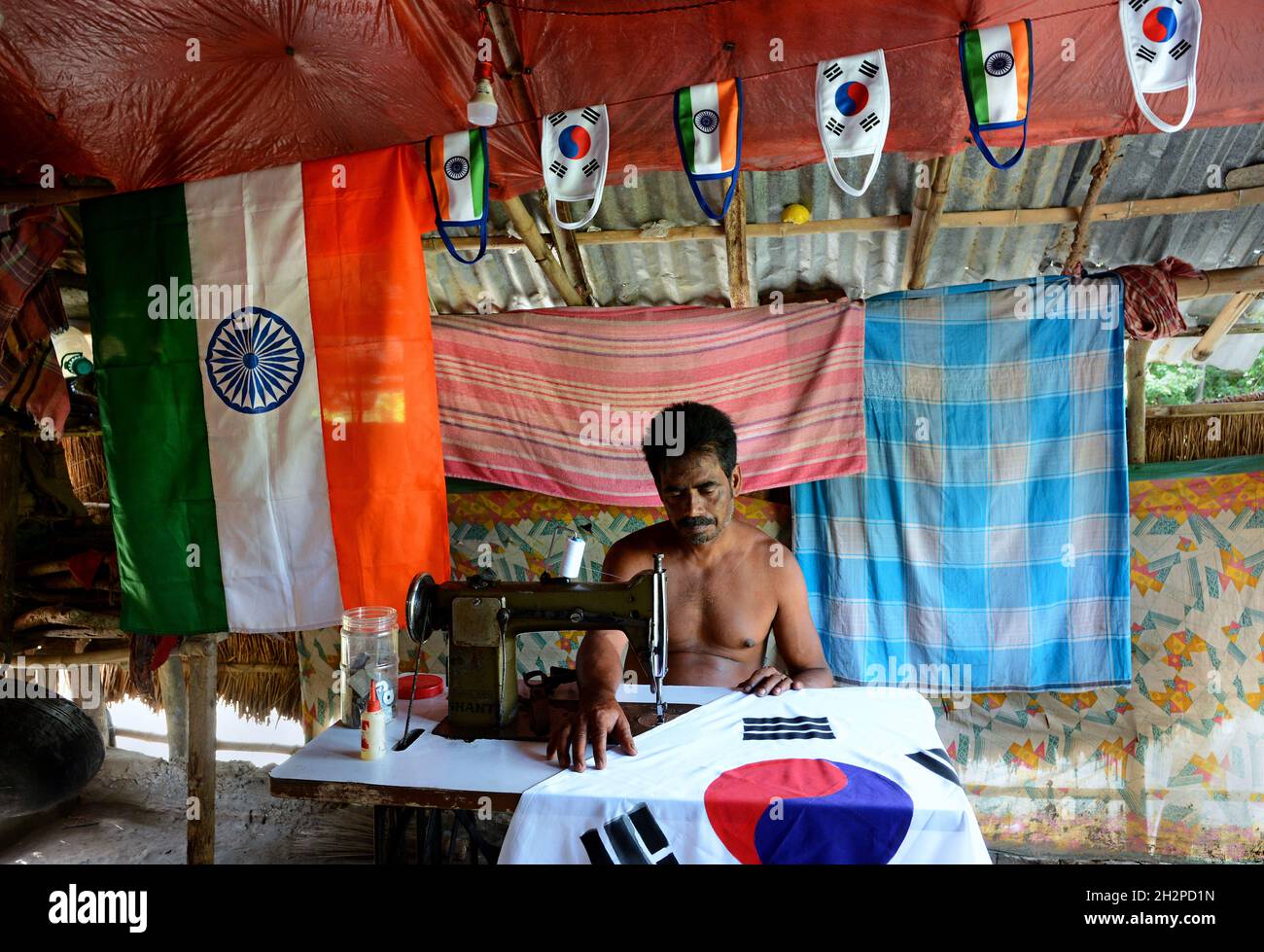Un sarto in quel villaggio remoto dell'India si era ingaggiare in bandiere e mascherare facendo sia per l'India che per la Corea del Sud in situazione pandemica in India. Foto Stock