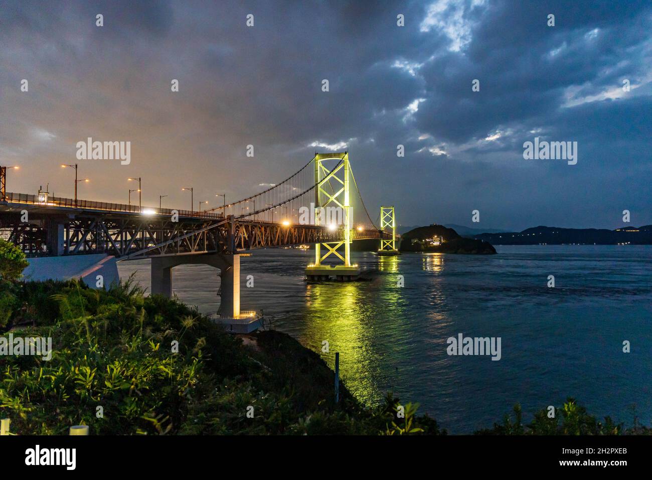 Le luci del ponte sospeso si mescolano con il bagliore del tramonto e le spettacolari nuvole Foto Stock