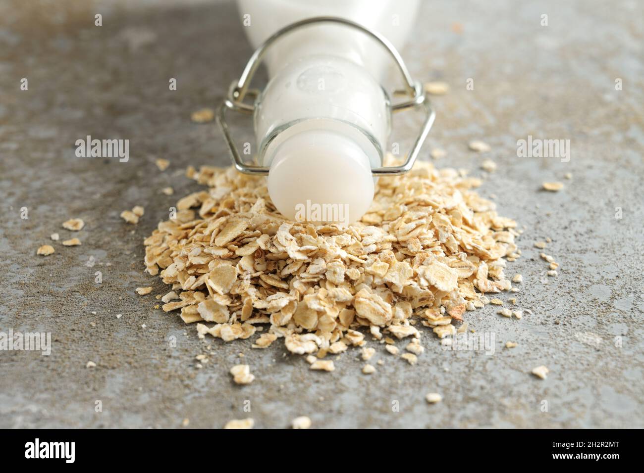 Latte di avena vegano, bottiglia con tappo si trova su un mucchio di farina d'avena su uno sfondo di pietra grigia, prodotto caseario alternativo, primo piano, spazio copia, selezionato Foto Stock