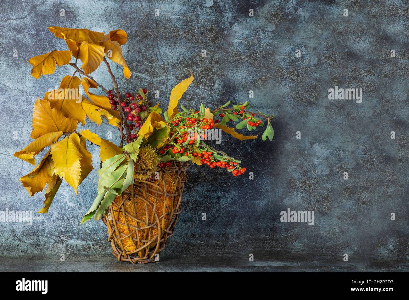 Autunno ikebana.Fall foglie di castagno giallo, rami con rosso selvatico e frutti di bosco di arancia in un cestino di vimini Foto Stock