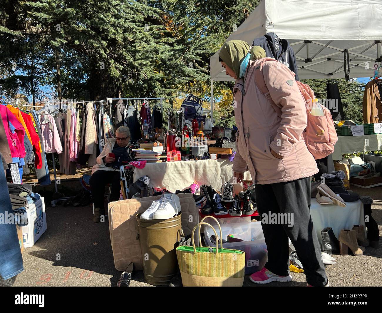 Donna che passeggera tra le bancarelle del mercato delle pulci con vestiti e scarpe di seconda mano. Sta ispezionando le merci e ha molto tempo il sabato di ottobre soleggiato. Foto Stock