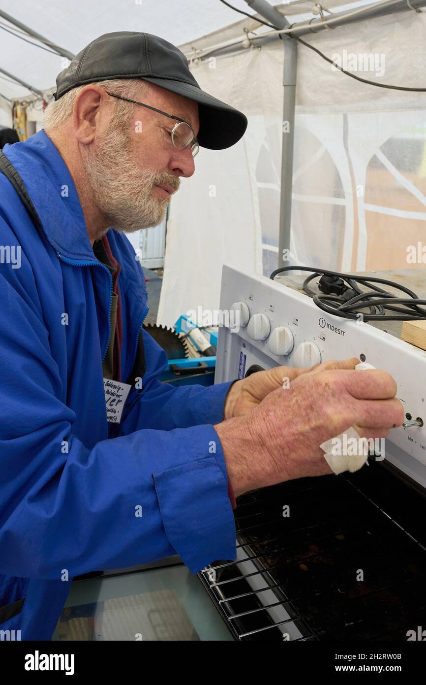Walporzheim, Germania. 21 ottobre 2021. 'Elektroseelsorger' Iwer ripara una stufa elettrica nella tenda dell'officina. L'associazione "Elektroseelsorge(r)", finanziata con donazioni, è composta da circa 220 elettricisti, tecnici delle telecomunicazioni e altri volontari provenienti da tutta la Germania. Si fangosi e una volta soddensi elettrodomestici come trapani, cacciaviti cordless, macchine da cucina e riscaldatori che funzionano di nuovo. (A dpa: ''Elektroseelsorge(r)' nella Valle dell'Ahr: 'Festival of Lights' as a Sign of Hope') Credit: Thomas Frey/dpa/Alamy Live News Foto Stock