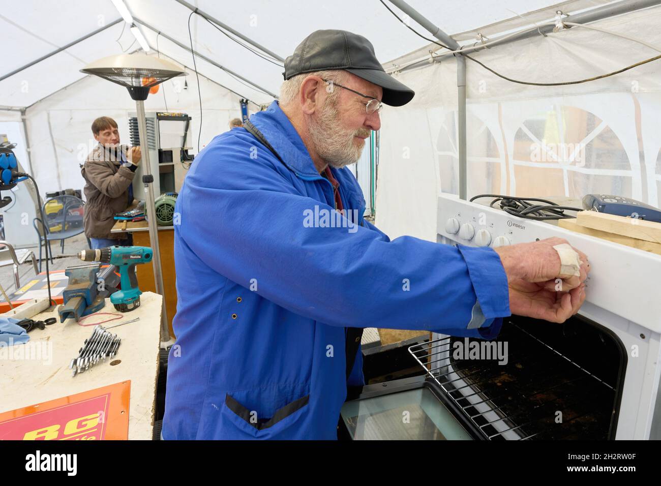 Walporzheim, Germania. 21 ottobre 2021. 'Elektroseelsorger' Iwer ripara una stufa elettrica nella tenda dell'officina. L'associazione "Elektroseelsorge(r)", finanziata con donazioni, è composta da circa 220 elettricisti, tecnici delle telecomunicazioni e altri volontari provenienti da tutta la Germania. Si fangosi e una volta soddensi elettrodomestici come trapani, cacciaviti cordless, macchine da cucina e riscaldatori che funzionano di nuovo. (A dpa: ''Elektroseelsorge(r)' nella Valle dell'Ahr: 'Festival of Lights' as a Sign of Hope') Credit: Thomas Frey/dpa/Alamy Live News Foto Stock
