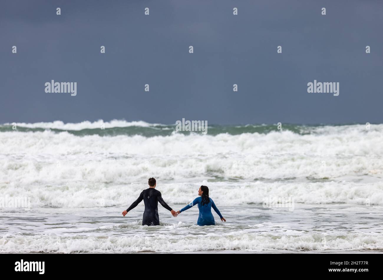 Nuotatori in tute bagnate che fanno surf sulla spiaggia di Polzeath North Cornwall, Regno Unito Foto Stock