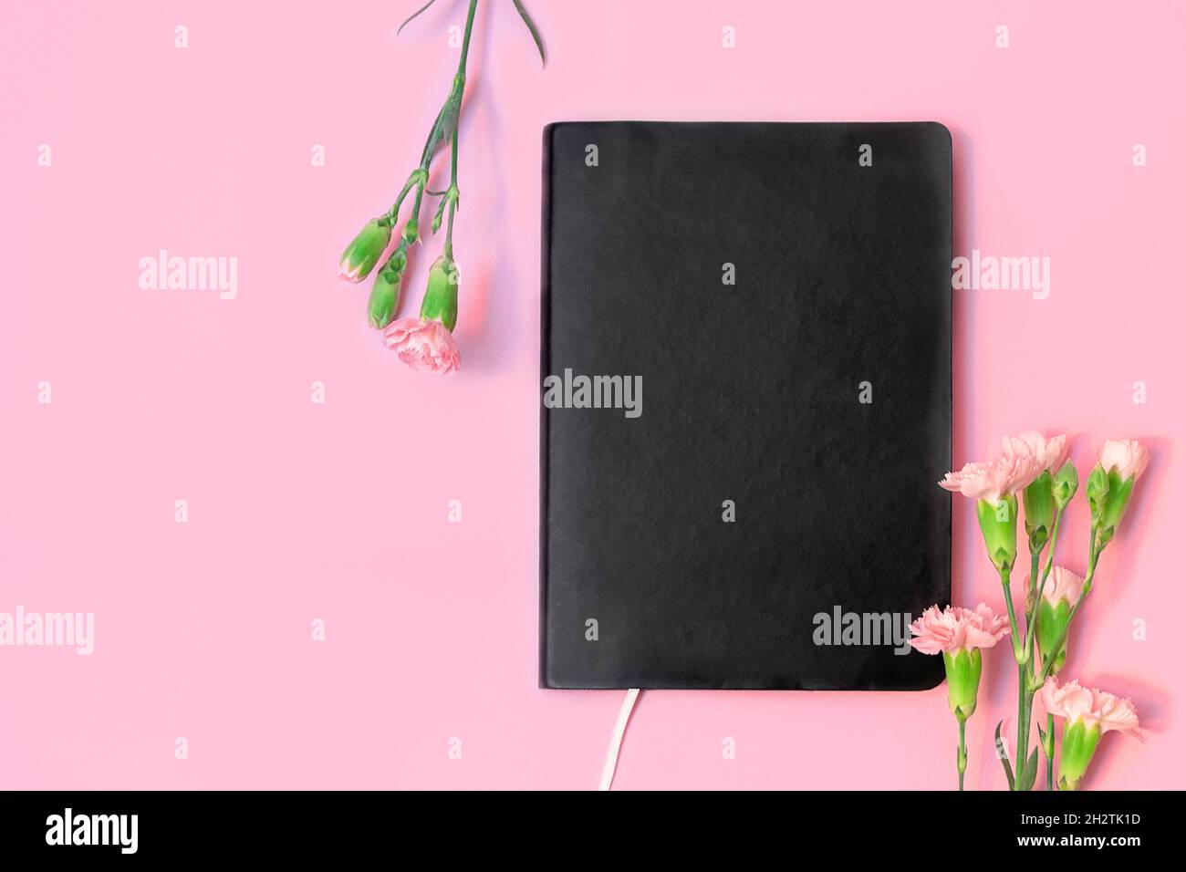 Vista dall'alto di un libro nero vuoto o di un taccuino e fiori su sfondo rosa pastello con spazio per la copia. Foto Stock